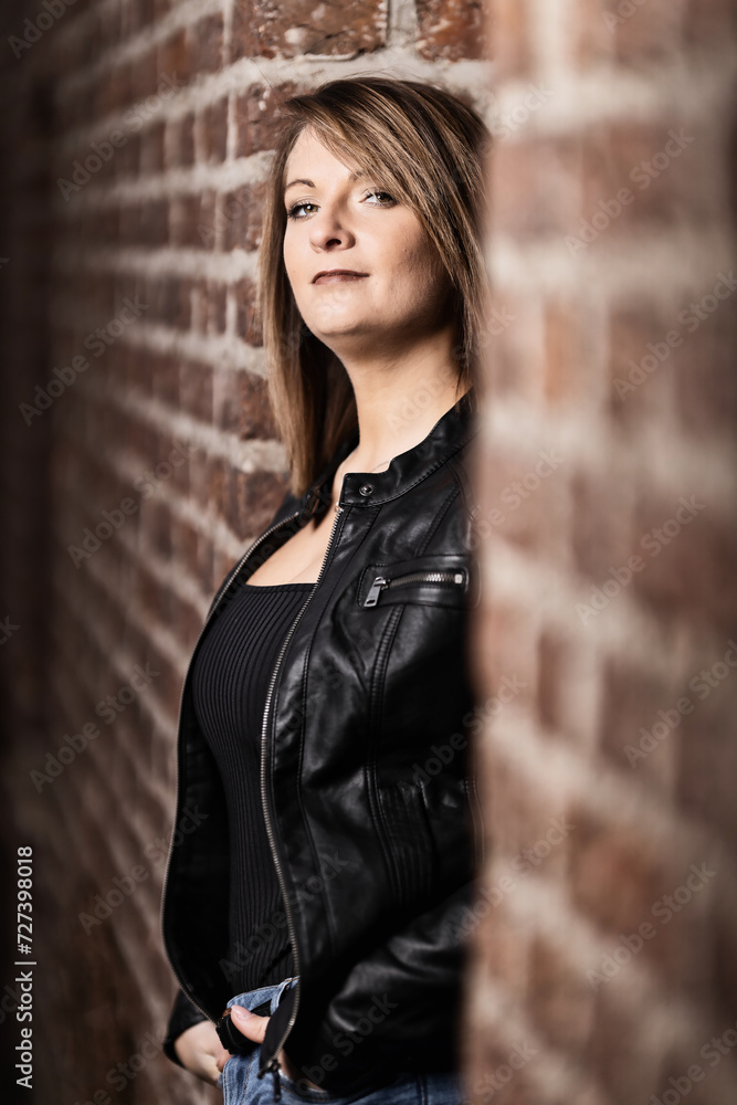 Woman model around thirty in black leather jacket and hot pants in front of urban brick wall. Woman model around thirty in black leather jacket and hot pants in front of urban brick wall.