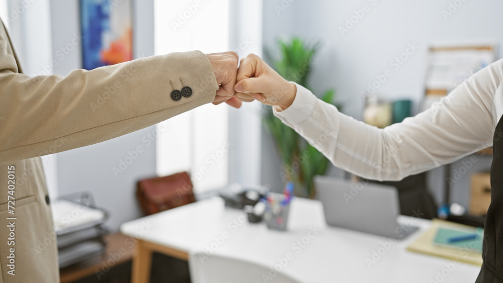 Two coworkers performing a fist bump in an office setting, signifying teamwork and partnership. Two coworkers performing a fist bump in an office setting, signifying teamwork and partnership.