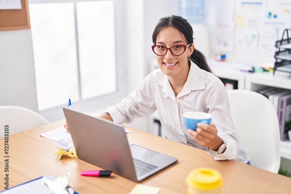 Young beautiful hispanic woman business worker writing on document drinking coffee at office Young beautiful hispanic woman business worker writing on document drinking coffee at office