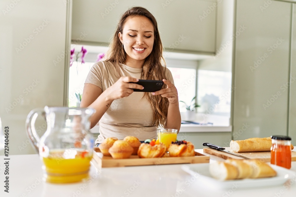 Young beautiful hispanic woman make photo by smartphone to breakfast at the kitchen