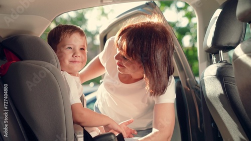 Mom gets her son out of car seat, safe car. Happy family. Mother unfastens her son in car seat with child seat belt. Family trip. Mom cares about her sons safety. Child sitting in a car child seat photo