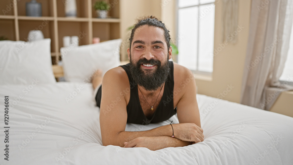 A cheerful bearded hispanic man relaxing in a modern bedroom, exuding a casual and welcoming atmosphere. A cheerful bearded hispanic man relaxing in a modern bedroom, exuding a casual and welcoming atmosphere.