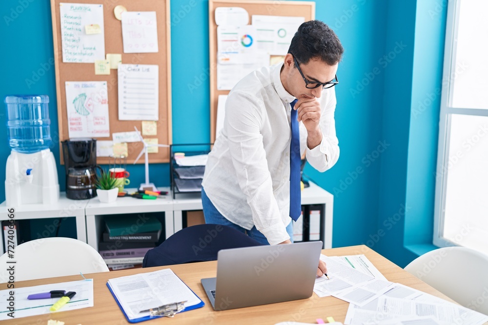 Young hispanic man business worker using laptop writing on document at office Young hispanic man business worker using laptop writing on document at office