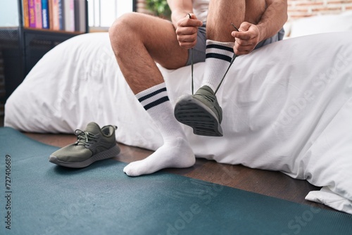 Young hispanic man tying sneaker at bedroom