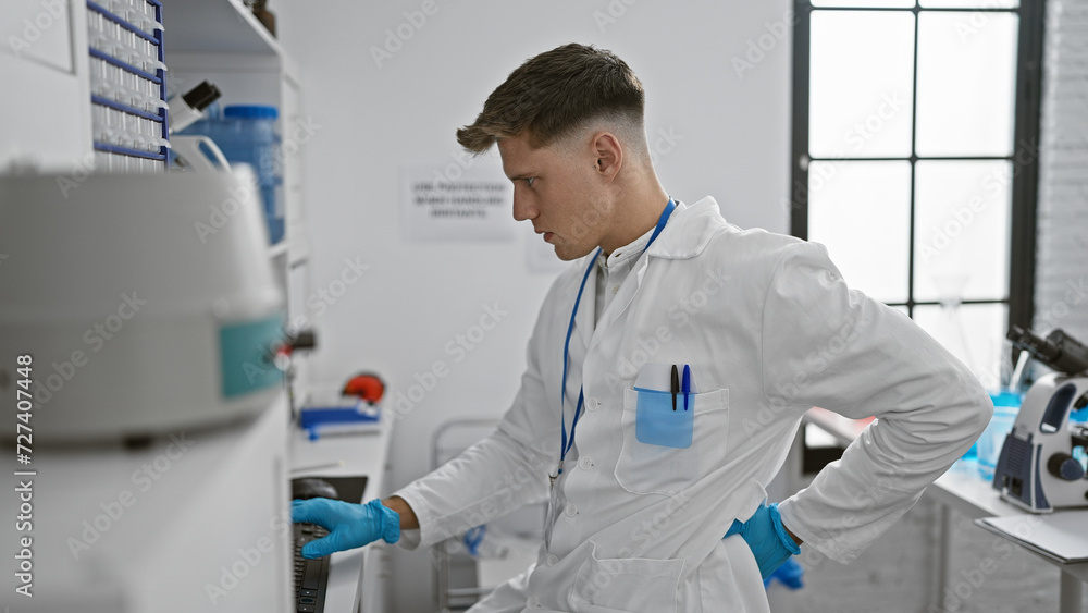 Naklejka premium Attractive young caucasian man scientist, typing away seriously on his computer at the lab, faces a plague of backache - a grim reality of research life.