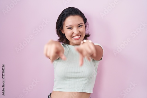 Hispanic young woman standing over pink background pointing to you and the camera with fingers, smiling positive and cheerful © Krakenimages.com