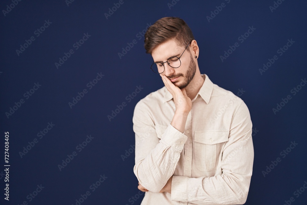 Hispanic man with beard standing over blue background thinking looking tired and bored with depression problems with crossed arms.