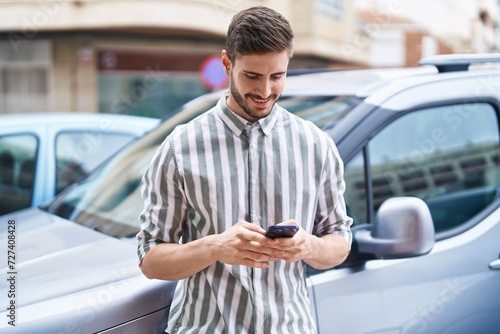 Young caucasian man using smartphone leaning on car at street