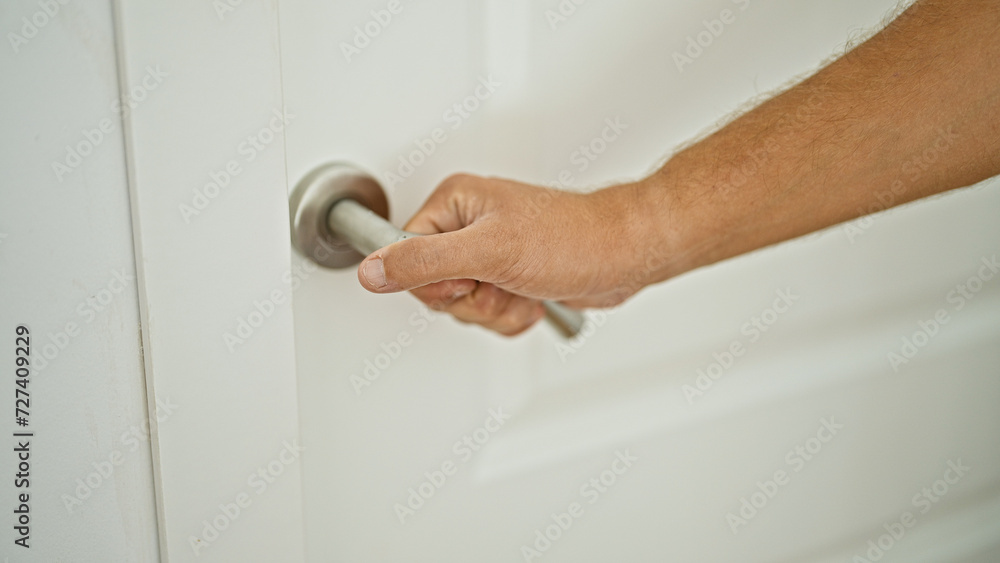 Obraz premium Closeup of a male hand gripping a modern doorknob to enter or exit a white interior room.