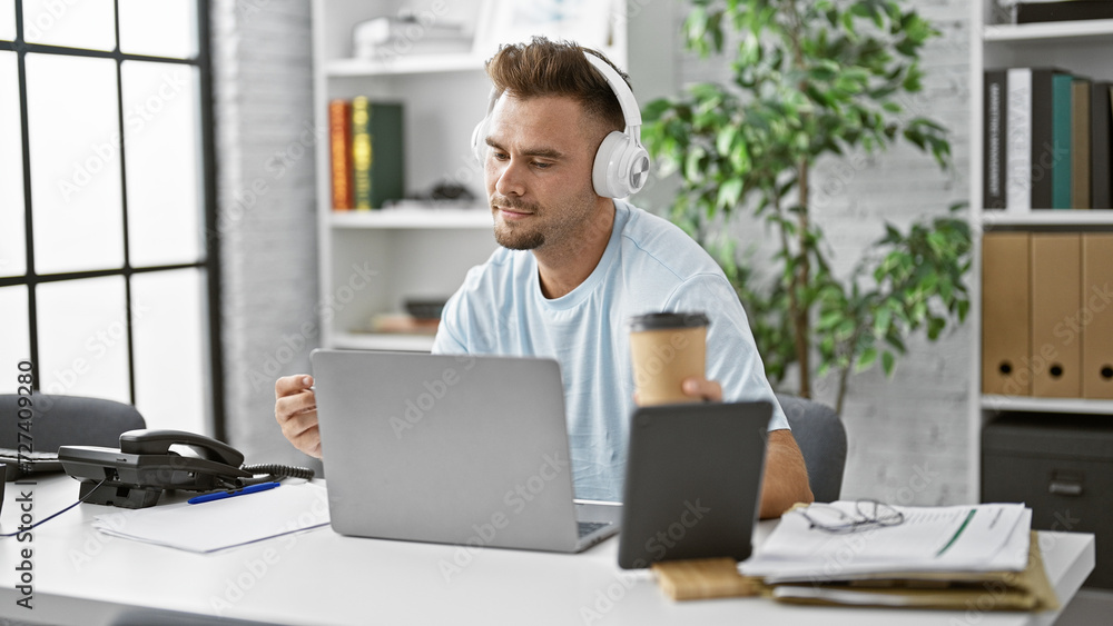 Hispanic man with beard wearing headphones concentrates on laptop in modern office. Hispanic man with beard wearing headphones concentrates on laptop in modern office.