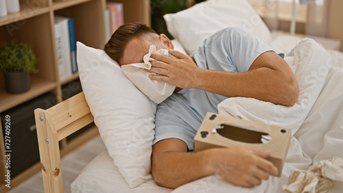 Crying hispanic man with a beard lying in bed at home, covering face with a tissue photo