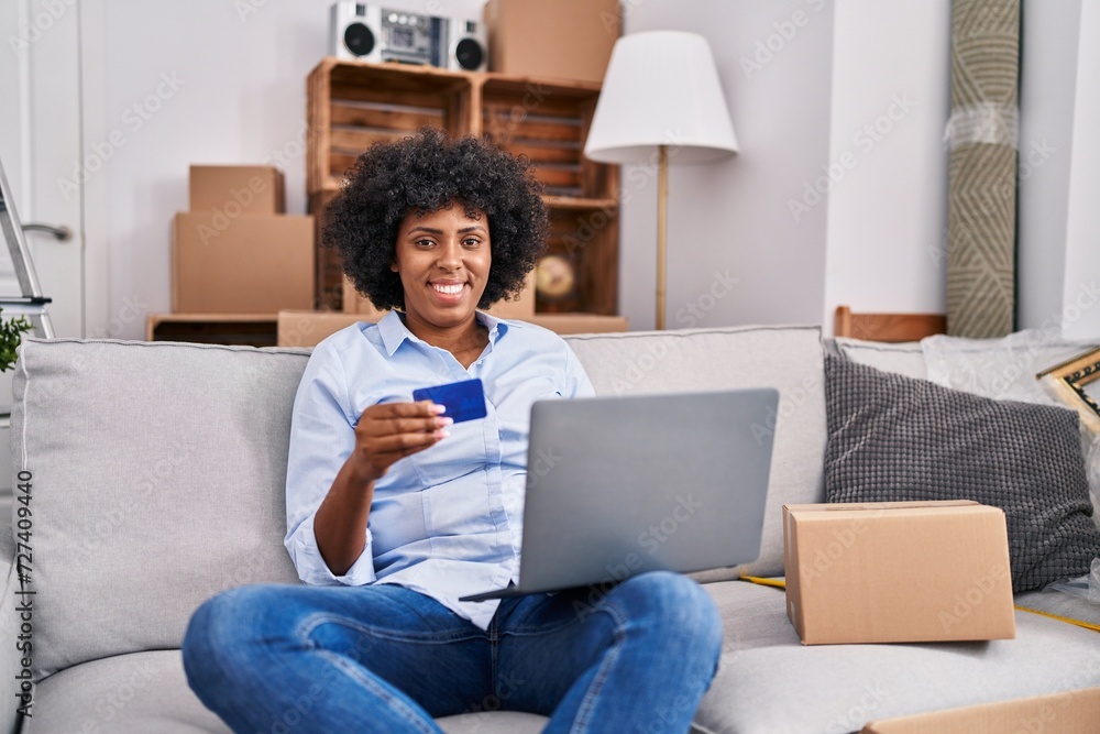 African american woman using laptop and credit card sitting on sofa at new home African american woman using laptop and credit card sitting on sofa at new home