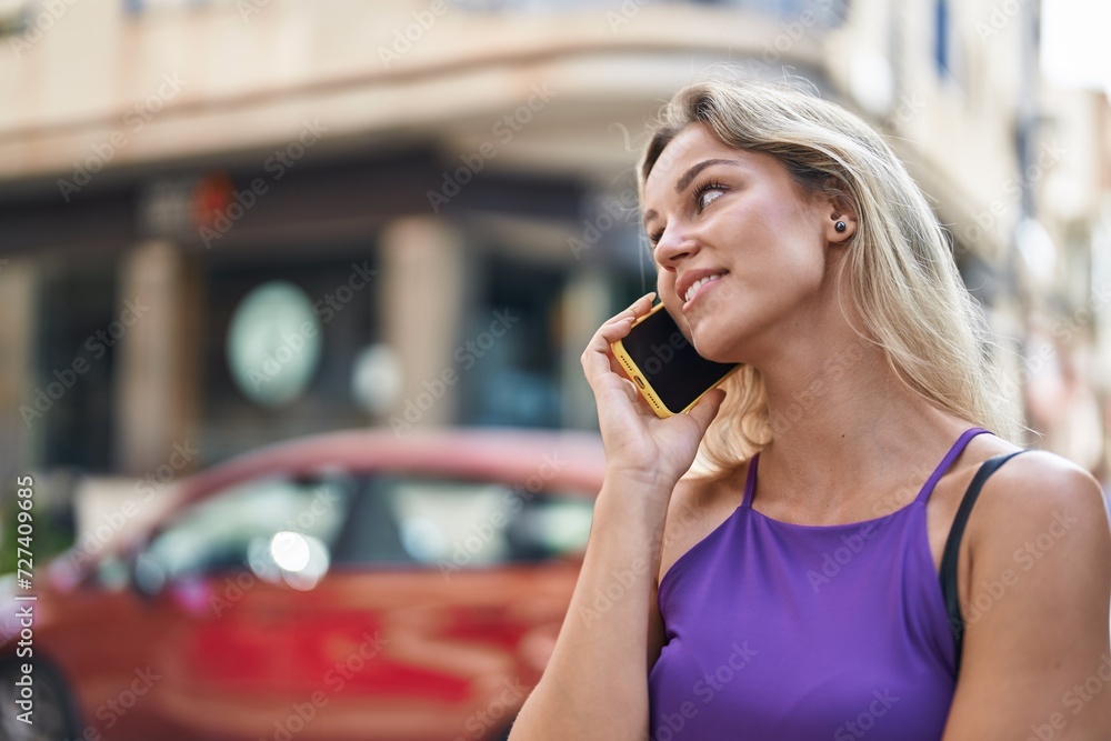 Fototapeta premium Young blonde woman smiling confident talking on the smartphone at street