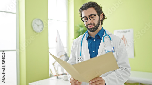 Young hispanic man doctor reading medical report at the clinic