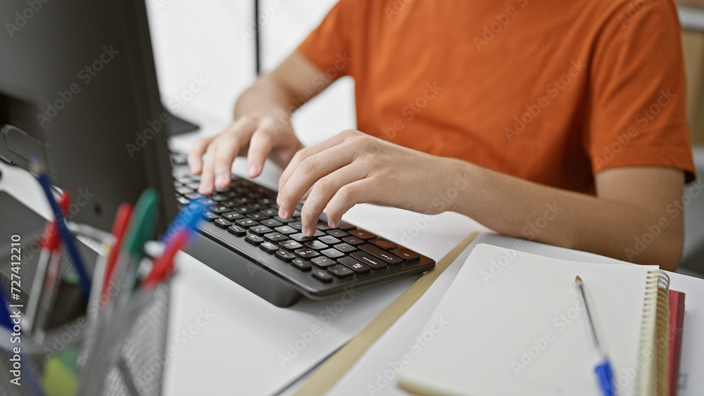 A young caucasian male teenager studying at a library table with a laptop, notebook, and pens, concentrating on his work. A young caucasian male teenager studying at a library table with a laptop, notebook, and pens, concentrating on his work.
