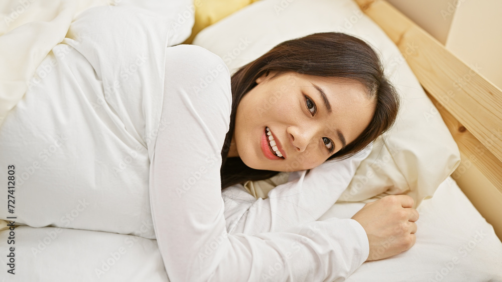A young asian woman smiling while lying comfortably in a bright bedroom setting. A young asian woman smiling while lying comfortably in a bright bedroom setting.