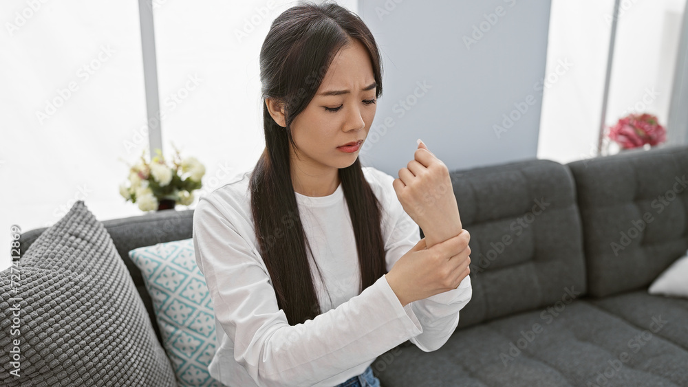 A pained young asian woman examines her wrist at home, suggesting discomfort or injury in a casual indoor setting. A pained young asian woman examines her wrist at home, suggesting discomfort or injury in a casual indoor setting.