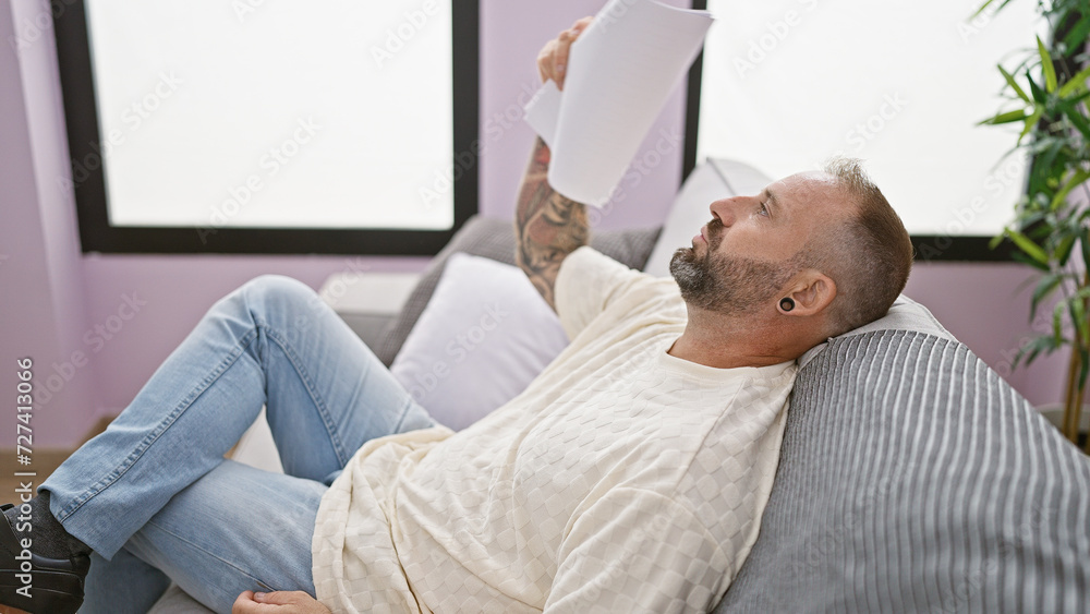 Hot weather torment, young man fanning himself with documents, suffering in a windless room, sitting on sofa at home Hot weather torment, young man fanning himself with documents, suffering in a windless room, sitting on sofa at home