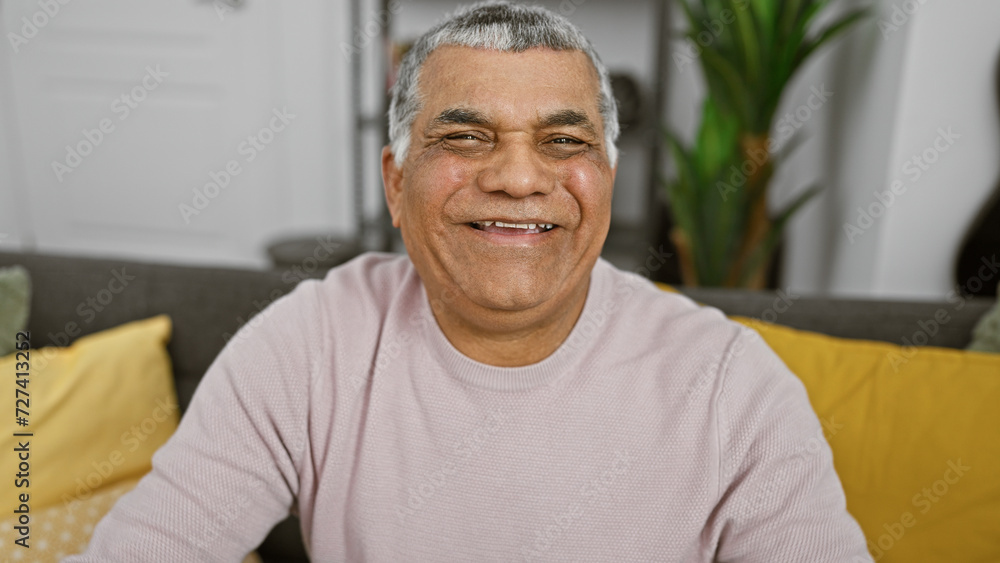 Fototapeta premium A smiling middle-aged man with grey hair, casually dressed, sits in a cozy, stylish living room.