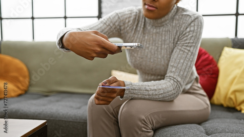 Young adult african american woman with curly hair photographing credit card indoors photo
