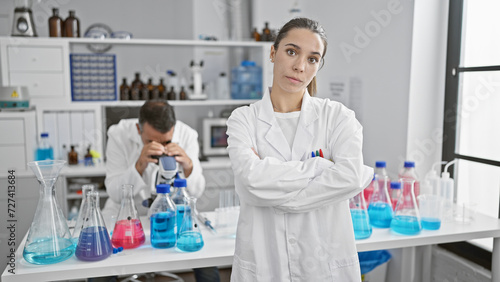 Fototapeta Naklejka Na Ścianę i Meble -  Two determined scientists, a man and woman, work together in a lab, portraying serious concentration with arms crossed gesture