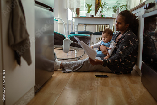 Single young mother holding her baby son going over bills and home finances in the kitchen at home photo
