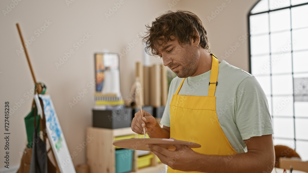 Focused man painting on canvas in a bright art studio wearing yellow apron. Focused man painting on canvas in a bright art studio wearing yellow apron.