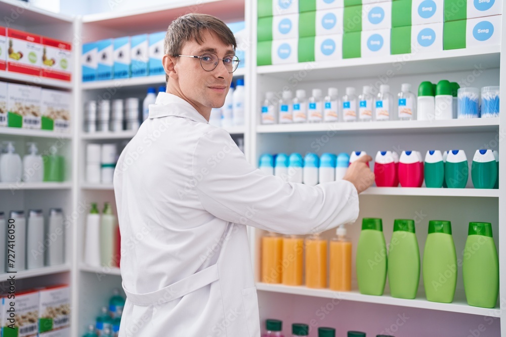 Young caucasian man pharmacist smiling confident holding product of shelving at pharmacy Young caucasian man pharmacist smiling confident holding product of shelving at pharmacy