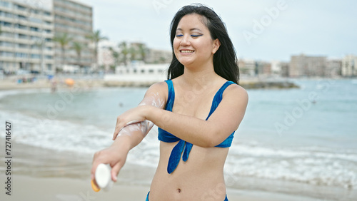 Fotografie Young chinese woman tourist wearing bikini applying sunscreen at the beach