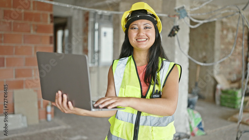 Young chinese woman architect using laptop smiling at construction site
