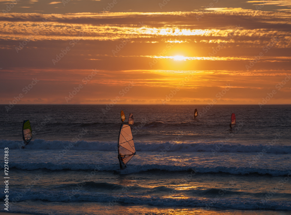 Windsurfers surfing in the atlantic during a golden sunset at sunset beach, Milnerton, Cape Town, South Africa