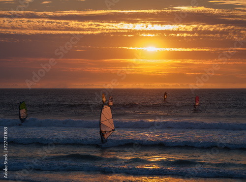 Windsurfers surfing in the atlantic during a golden sunset at sunset beach, Milnerton, Cape Town, South Africa photo