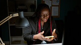 Exhausted african american business woman stressed out at work, texting problems away on smartphone in dark office room