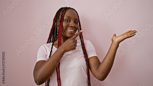 Joyful african american woman confidently presenting, pointing to the side with a beatific smile over an isolated pink background