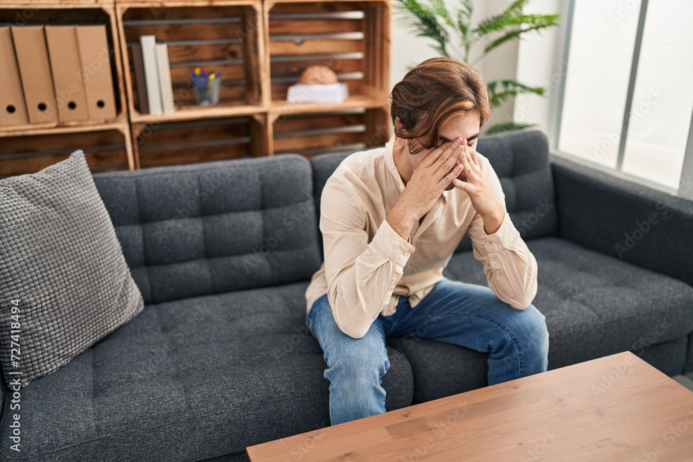 Young caucasian man patient stressed sitting on sofa at psychology clinic
