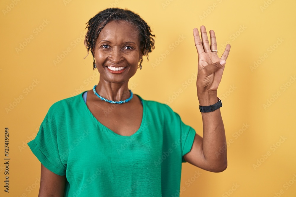 African woman with dreadlocks standing over yellow background showing and pointing up with fingers number four while smiling confident and happy. African woman with dreadlocks standing over yellow background showing and pointing up with fingers number four while smiling confident and happy.