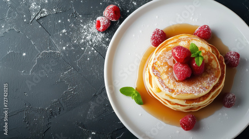 stack of golden pancakes decorated with raspberries and powdered sugar on dark stone table , top view  photo