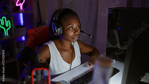 Focused woman gaming indoors at night with headset in a neon-lit room.