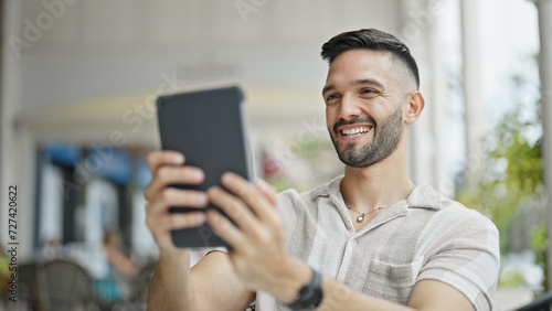 Young hispanic man smiling confident using touchpad at coffee shop terrace