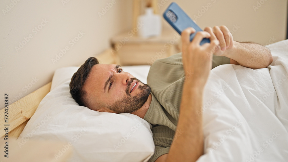 Young hispanic man using smartphone lying on bed at bedroom Young hispanic man using smartphone lying on bed at bedroom