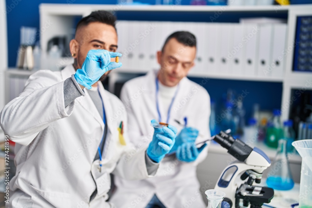 Two men scientist writing on document holding pills at laboratory Two men scientist writing on document holding pills at laboratory