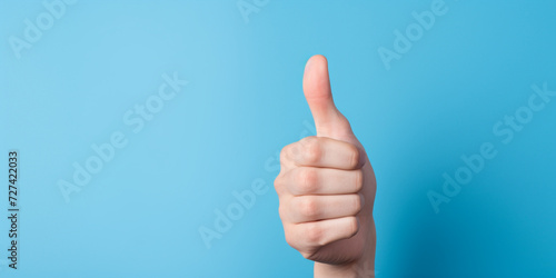 Hand makes thumbs up gesture on blue background. The gesture is all good, like.