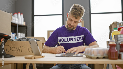 Caucasian volunteer man writing in a warehouse filled with food and clothing donations.