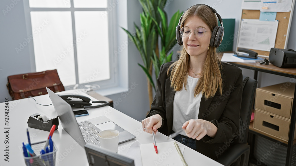 A professional young woman wearing glasses and headphones focused on her work in a modern office setting A professional young woman wearing glasses and headphones focused on her work in a modern office setting