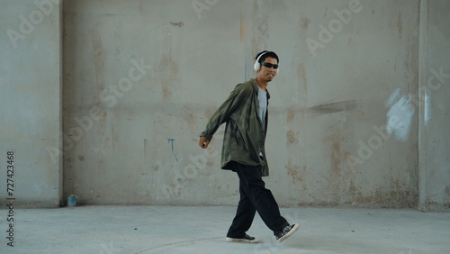 Hipster wearing headphone while listen hip-hop music at city street. Street dancer moving footstep to music from headphone. Outdoor sport 2024. Cement background. Fashion. Active style. Endeavor. © Summit Art Creations