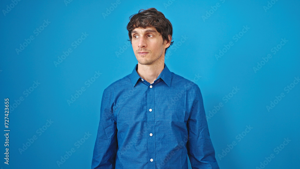 Young hispanic man looking to the side with serious expression over isolated blue background Young hispanic man looking to the side with serious expression over isolated blue background