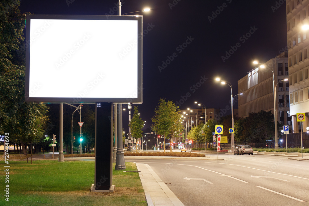 Large horizontal billboard in the night city. Bright lights of lanterns on poles near the road. Mock-up.