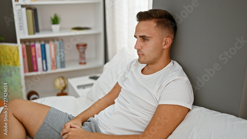 Obraz na plátně Handsome thoughtful man sitting indoors wearing casual clothing in a cozy room setting contemplating