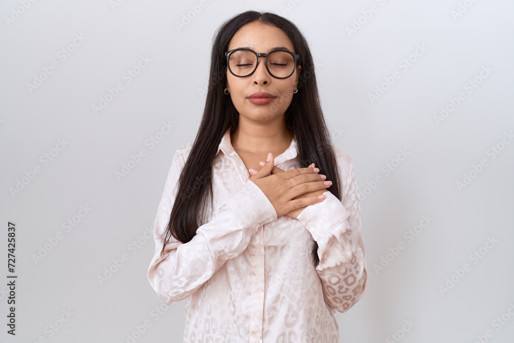 Young arab woman wearing glasses over white background smiling with hands on chest with closed eyes and grateful gesture on face. health concept.