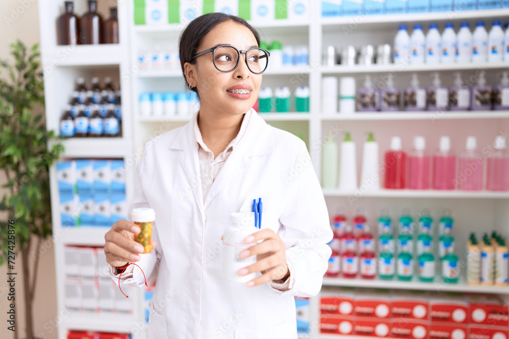Young arab woman pharmacist smiling confident holding pills bottles at pharmacy
